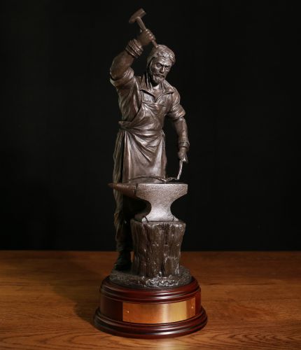 Blacksmith, Armourer and Craftsman. This is a 12" scale sculpture depicting a Blacksmith forging and beating out piece of metal. We complete the sculpture with a choice of finish, a wooden base and a fully engraved nameplate on the front of the base.