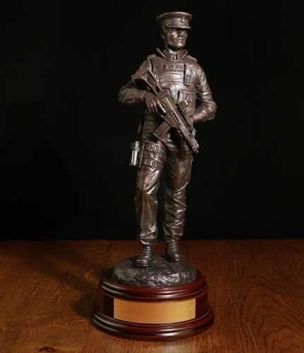 A bronze cold cast resin statue of a Modern Male British Armed Police officer on foot patrol. He's wearing a police issue flat style cap. We include the standard wooden base and an engraved brass plate
