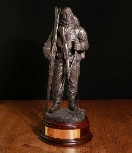 12" scale cold cast bronze resin sculpture of a Royal Marine Commando dressed for arctic warfare with Skis and poles. His SLR Rifle is slung down across his chest. We offer a choice of wooden bases and finishes